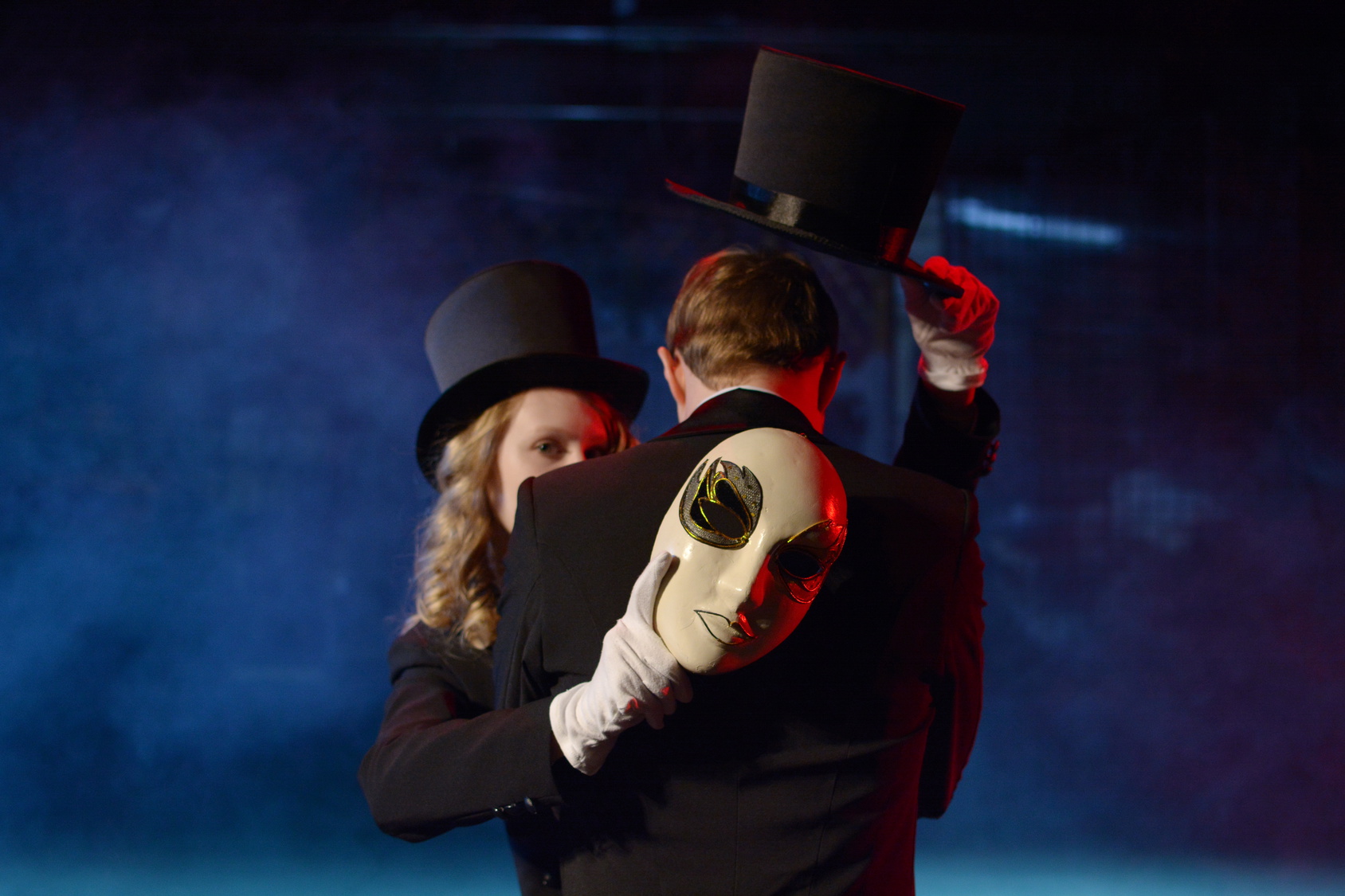 man and woman dancing in tuxedos and holding a theatrical mask